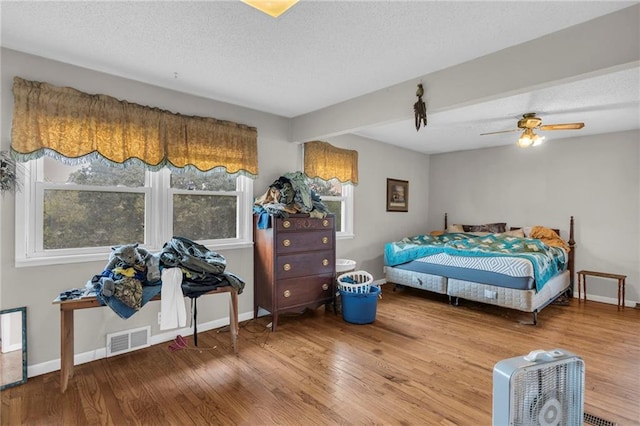 bedroom featuring a textured ceiling, beam ceiling, hardwood / wood-style floors, and ceiling fan