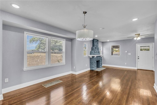 unfurnished living room with dark hardwood / wood-style flooring, ceiling fan, and a stone fireplace