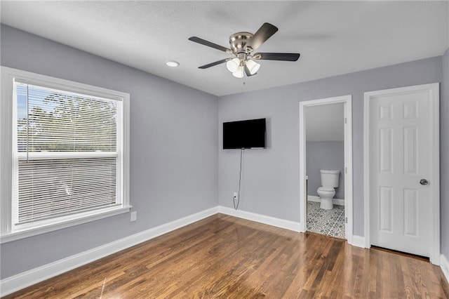 unfurnished bedroom featuring a closet, connected bathroom, ceiling fan, and dark wood-type flooring