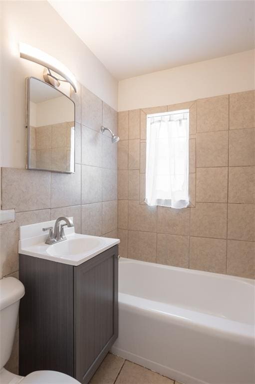 full bathroom with tile walls, tiled shower / bath, vanity, and toilet