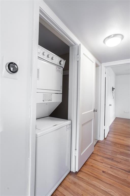 washroom with stacked washing machine and dryer and light wood finished floors