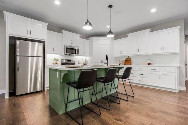 kitchen with wood finished floors, an island with sink, stainless steel appliances, light countertops, and backsplash