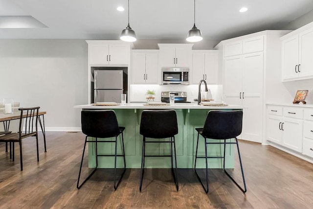 kitchen featuring a sink, an island with sink, light countertops, baseboards, and appliances with stainless steel finishes
