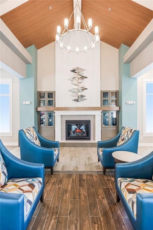 sitting room with wood finished floors, wooden ceiling, a glass covered fireplace, high vaulted ceiling, and a notable chandelier