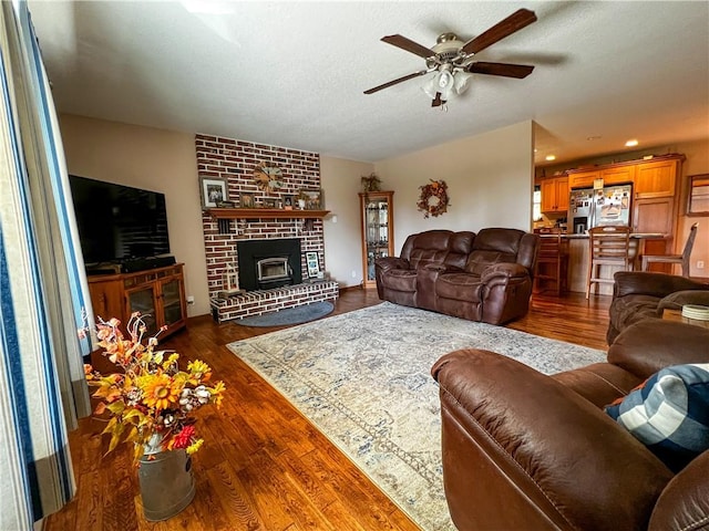 living room with a textured ceiling, a fireplace, dark hardwood / wood-style floors, and ceiling fan