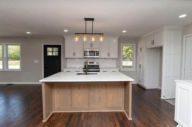 kitchen with appliances with stainless steel finishes, light stone countertops, a kitchen island with sink, and dark hardwood / wood-style flooring