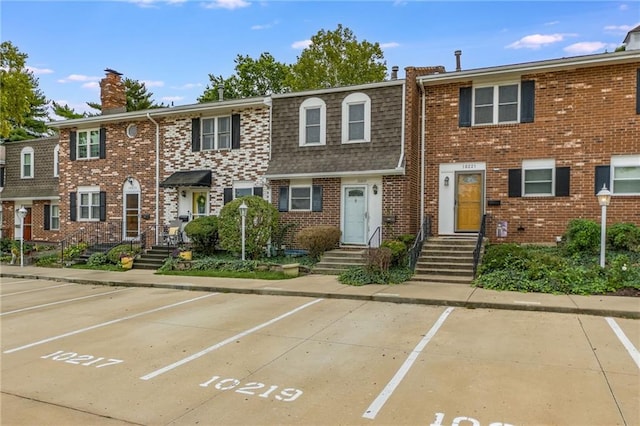 view of property with roof with shingles, uncovered parking, mansard roof, and brick siding