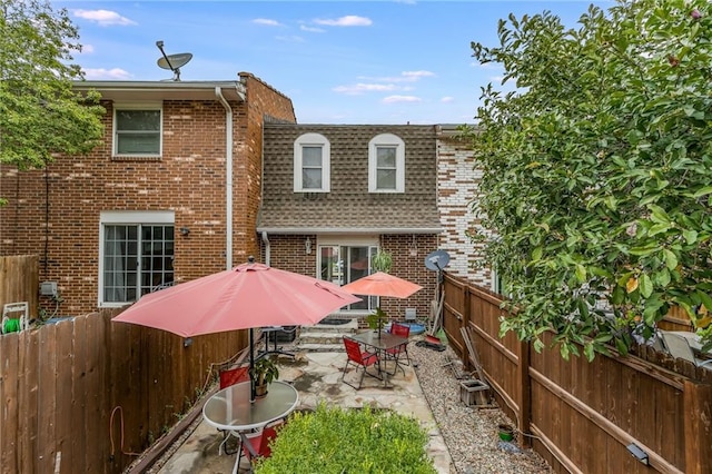 back of house with brick siding, mansard roof, a shingled roof, a patio area, and a fenced backyard