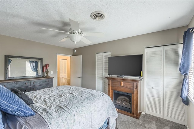 bedroom featuring carpet floors, multiple closets, visible vents, ceiling fan, and a textured ceiling