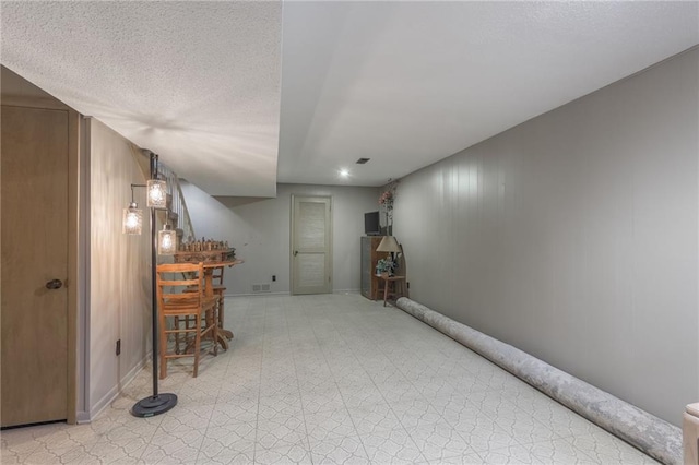 finished basement with a dry bar, light floors, baseboards, and a textured ceiling