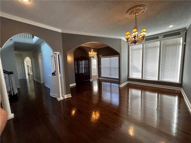 unfurnished dining area with a textured ceiling, an inviting chandelier, dark hardwood / wood-style flooring, ornamental molding, and ornate columns