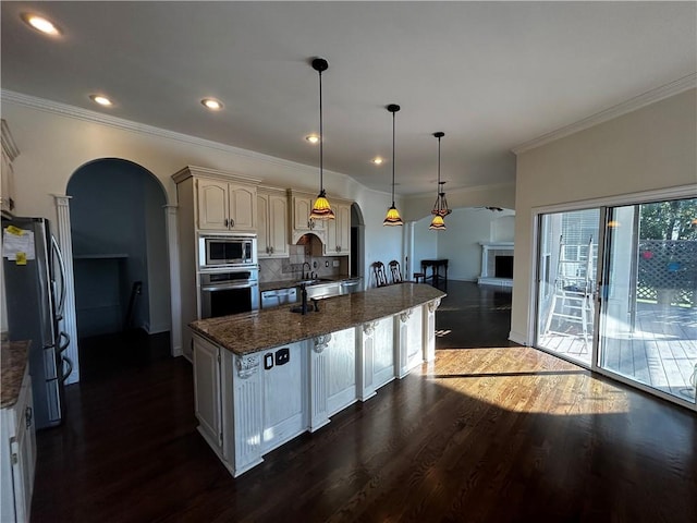 kitchen with hanging light fixtures, tasteful backsplash, stainless steel appliances, dark hardwood / wood-style floors, and dark stone countertops