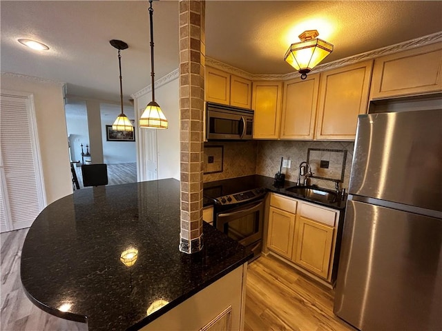 kitchen featuring appliances with stainless steel finishes, hanging light fixtures, dark stone countertops, light hardwood / wood-style flooring, and sink