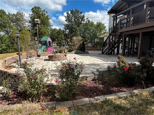 view of playground with a wooden deck, a patio area, and a fire pit