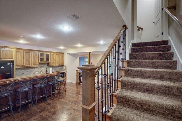 4602 NW Verona Dr, Riverside, MO 64150 - kitchen featuring a breakfast bar, dark wood-style floors, glass insert cabinets, freestanding refrigerator, and backsplash