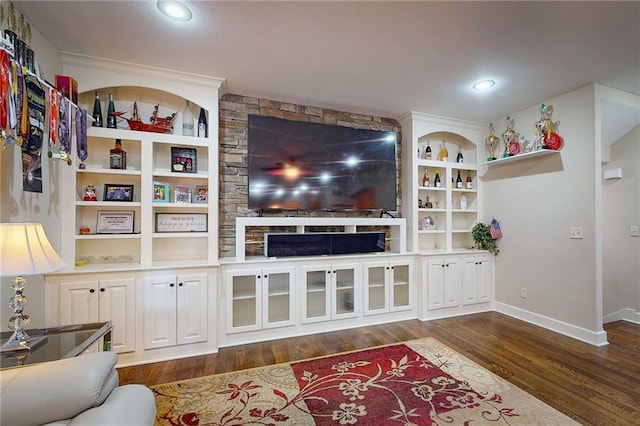 living room with built in shelves, a stone fireplace, and dark hardwood / wood-style flooring