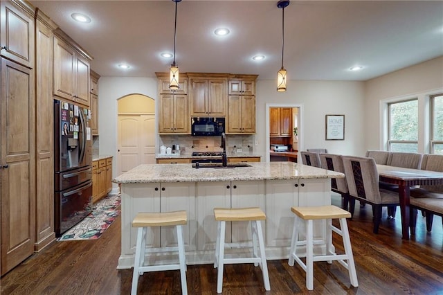 kitchen with pendant lighting, an island with sink, black appliances, light stone countertops, and dark hardwood / wood-style flooring