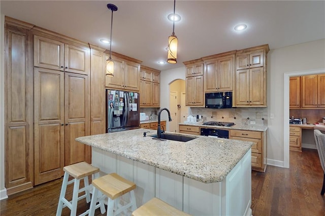 kitchen with light stone counters, tasteful backsplash, hanging light fixtures, black appliances, and a center island with sink