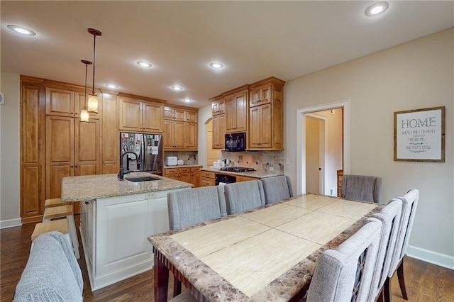 kitchen featuring sink, decorative light fixtures, a kitchen island with sink, appliances with stainless steel finishes, and decorative backsplash