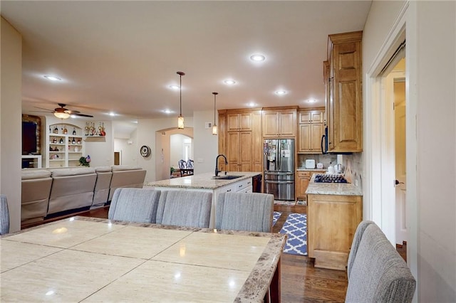 kitchen featuring hanging light fixtures, an island with sink, wood-type flooring, ceiling fan, and stainless steel refrigerator with ice dispenser