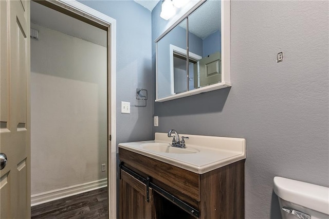 bathroom with toilet, a textured ceiling, wood finished floors, vanity, and a textured wall