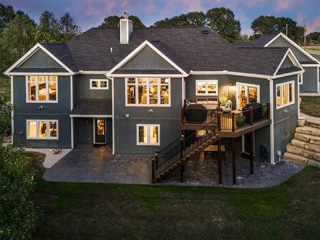 back house at dusk with a patio, a lawn, and a wooden deck