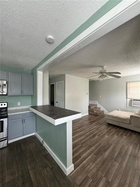 kitchen featuring dark hardwood / wood-style floors, kitchen peninsula, stainless steel appliances, a textured ceiling, and ceiling fan