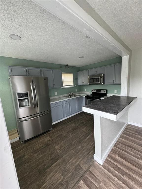 kitchen featuring gray cabinetry, a textured ceiling, dark hardwood / wood-style flooring, kitchen peninsula, and stainless steel appliances