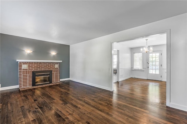 unfurnished living room featuring a notable chandelier, a brick fireplace, and dark hardwood / wood-style floors