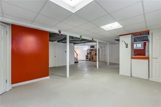 basement with stainless steel refrigerator and a paneled ceiling