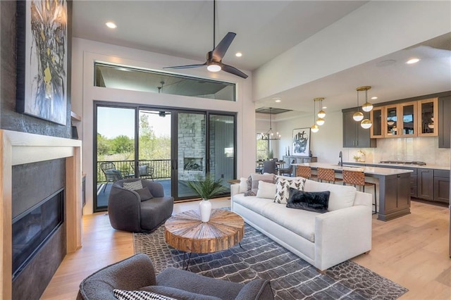 living room featuring ceiling fan with notable chandelier, light hardwood / wood-style floors, and sink