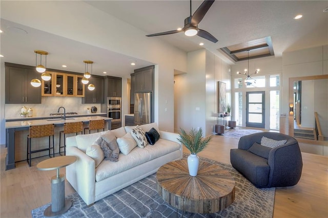 living room with ceiling fan with notable chandelier, light hardwood / wood-style floors, and sink