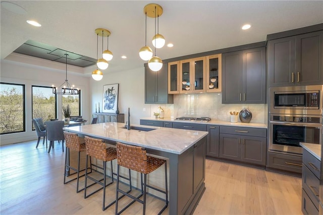 kitchen featuring appliances with stainless steel finishes, hanging light fixtures, an island with sink, sink, and a notable chandelier