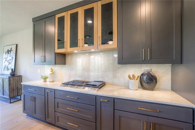 kitchen featuring gray cabinets, light stone counters, stainless steel gas cooktop, light hardwood / wood-style flooring, and backsplash