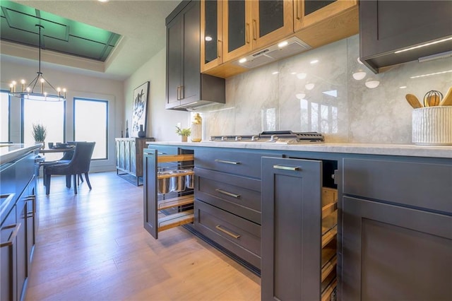 kitchen featuring hanging light fixtures, light hardwood / wood-style floors, decorative backsplash, stainless steel gas cooktop, and a chandelier