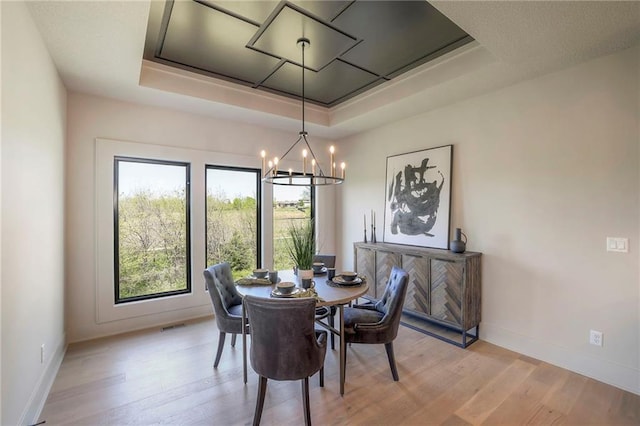 dining space with a raised ceiling, a chandelier, and light hardwood / wood-style flooring