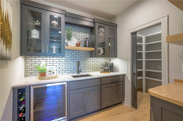 bar featuring sink, gray cabinetry, beverage cooler, light wood-type flooring, and decorative backsplash