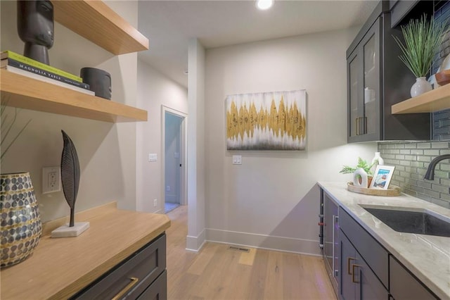 kitchen with gray cabinets, light stone counters, tasteful backsplash, sink, and light hardwood / wood-style flooring