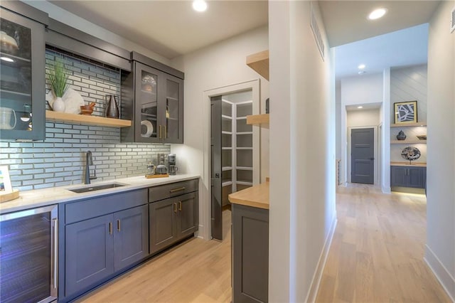 kitchen featuring light wood-type flooring, decorative backsplash, sink, and wine cooler