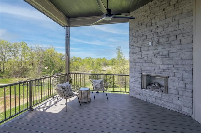 deck featuring ceiling fan and an outdoor stone fireplace