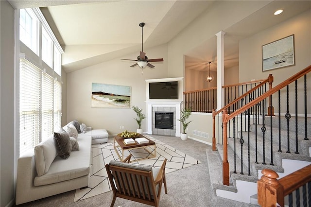 carpeted living room with a tile fireplace, ceiling fan, and high vaulted ceiling