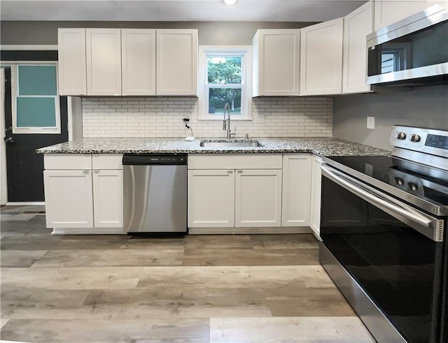 kitchen with white cabinetry, appliances with stainless steel finishes, light stone counters, and sink