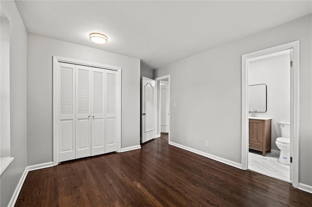 unfurnished bedroom with ensuite bathroom, a closet, and dark hardwood / wood-style floors