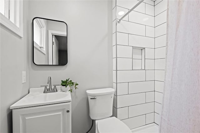 bathroom featuring a tile shower, vanity, and toilet