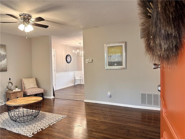 sitting room with a textured ceiling, ceiling fan with notable chandelier, and dark hardwood / wood-style flooring