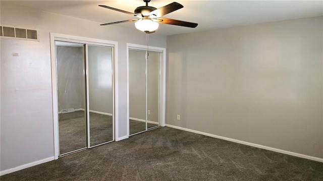 unfurnished bedroom featuring ceiling fan, multiple closets, and dark carpet