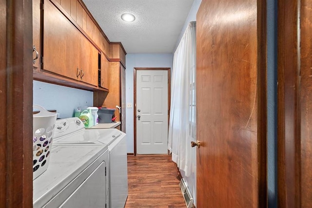 washroom with a textured ceiling, washing machine and dryer, dark wood-type flooring, and cabinets