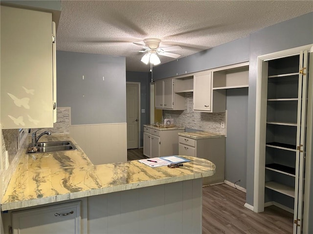 kitchen featuring ceiling fan, sink, kitchen peninsula, a textured ceiling, and dark hardwood / wood-style floors