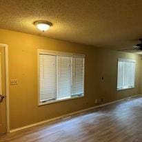 empty room with a textured ceiling, wood-type flooring, and ceiling fan