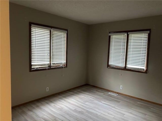 spare room featuring a textured ceiling and light hardwood / wood-style floors